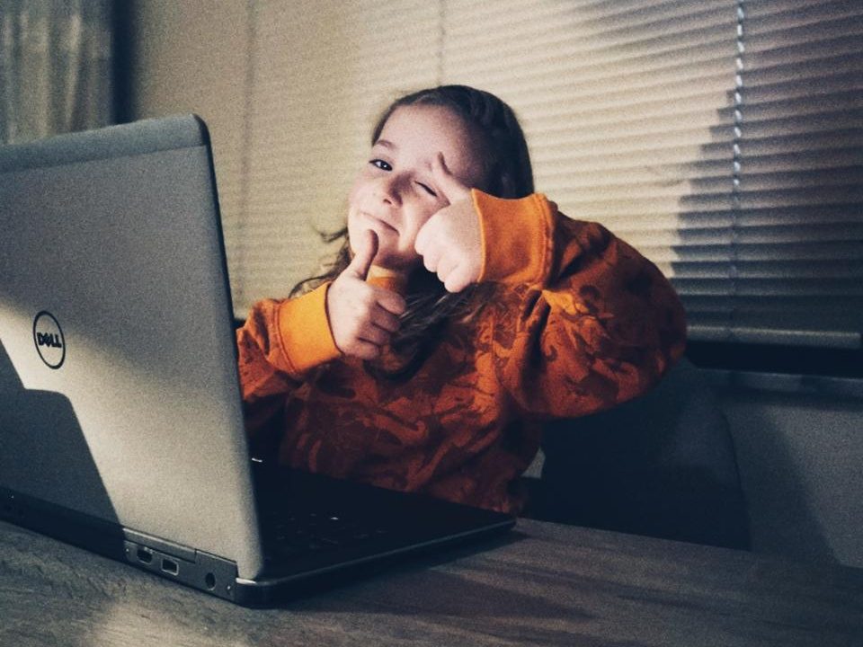 A child giving a thumbs-up beside a laptop